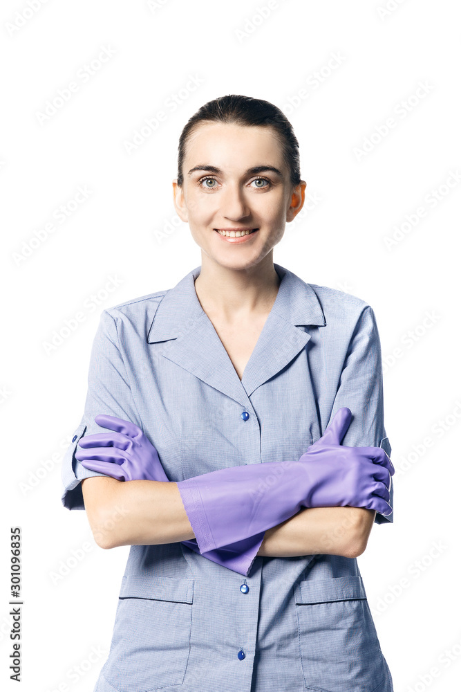 A beautiful young woman in the uniform of a maid smiling crossed her hands in rubber gloves on her chest. Isolated on a white background.