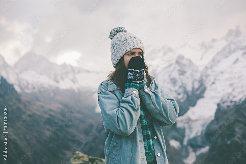 Young traveler girl in gloves standing over mountain peaks and warming cold hands