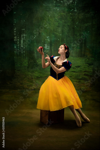 Young ballet dancer as a Snow White with poisoned apple in forest. Flexible caucasian ballerina dances like character of fairytail in bright clothes. Adorable and elegance story in motion and dancing.