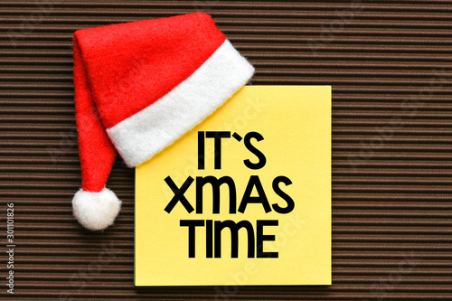It`s xmas time text on a yellow card with a Santa hat.