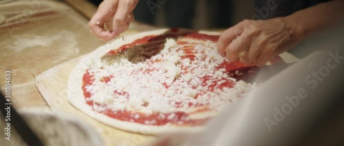 Chef spreading cheese on ready traditional italian pizza dough with tomato sauce in kitchen of restaurant. Slow motion, shot with Blackmagic Design Pocket Cinema Camera 4K 