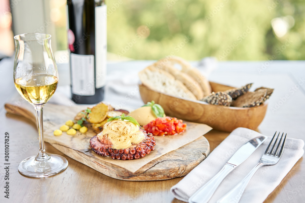 Roasted octopus BBQ and Baked potato with a glass of Grapa. Wooden plate. Restaurant menu