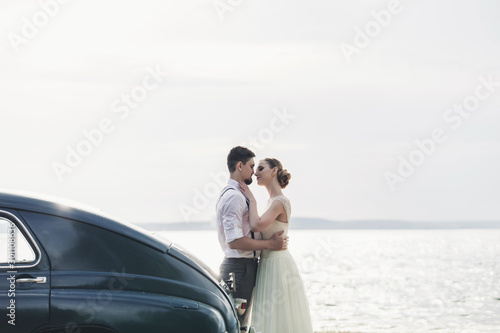 Billede på lærred Happy bride and groom standing near car on shore sea