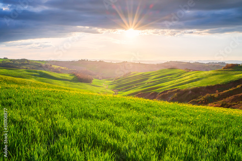 Amazing spring landscape with sun's rays touching the endless green rolling hills of Tuscany at sunrise