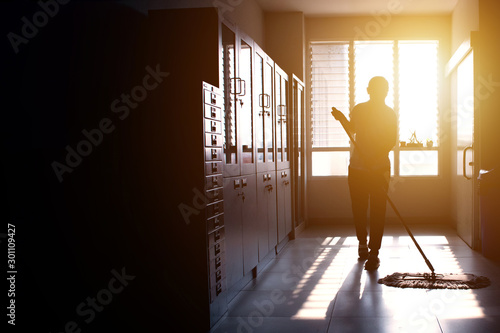Janitor woman mopping floor in hallway office building or walkway after school or classroom with copy space. Silhouette housekeeper working job with sun light background. photo