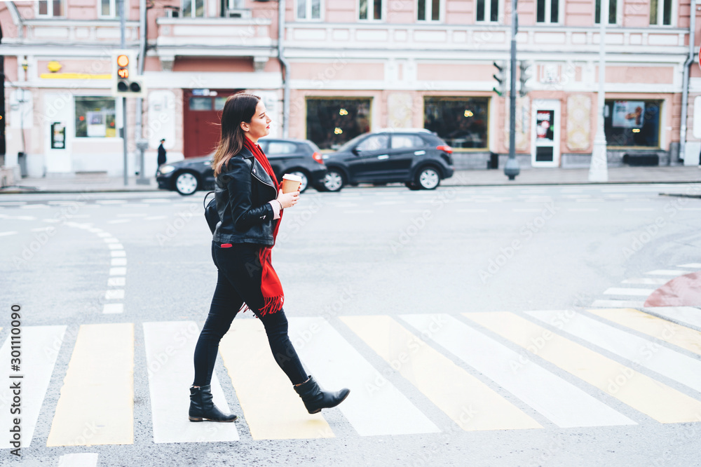 parallel Aannames, aannames. Raad eens Onnodig A beautiful brunette woman crosses the road on pedestrian crossing in a  black leather jacket and a red scarf and hold in hand a hot drink. Stock  Photo | Adobe Stock