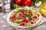 Vegetable salad of white onion, cucumber, tomatoes, lettuce, parsley on grey concrete background. Low carb dietary food.