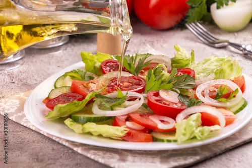 Vegetable salad of white onion  cucumber  tomatoes  lettuce  parsley on grey concrete background. Low carb dietary food. olive oil pouring from jar.
