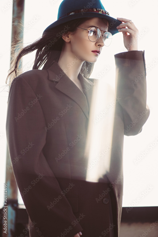 elegant fashionable woman posing in hat, eyeglasses and brown jacket on roof elegant fashionable woman posing in hat, eyeglasses and brown jacket on roof
