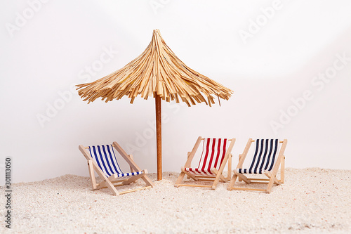 Photographie Toy chaise longue and sun umbrella on sandy beach on sunny day at the white background