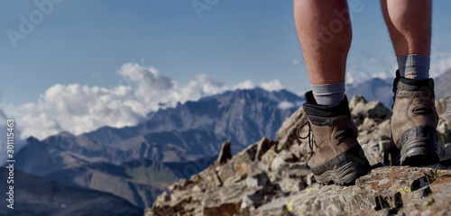 Close up view of high trekking boots and male legs on stony mountain top; dangerous hiking route with professional reliable equipment; wide panorama for banner; space for text