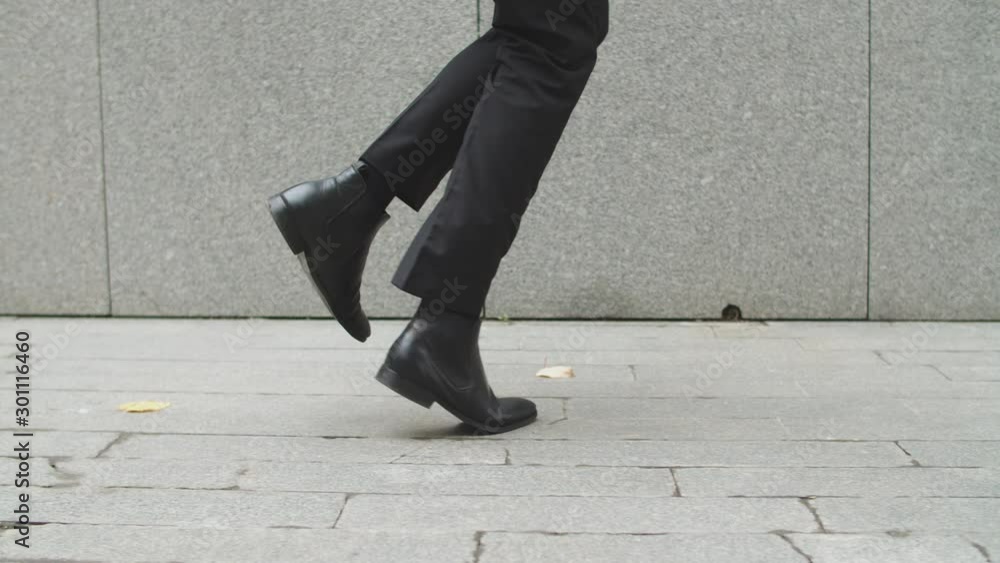 Close up male legs walk in city. Unrecognizable elegant guy walking along the sidewalk. Person wearing elegant black suit and shoes Close up male legs walk in city. Unrecognizable elegant guy walking along the sidewalk. Person wearing elegant black suit and shoes