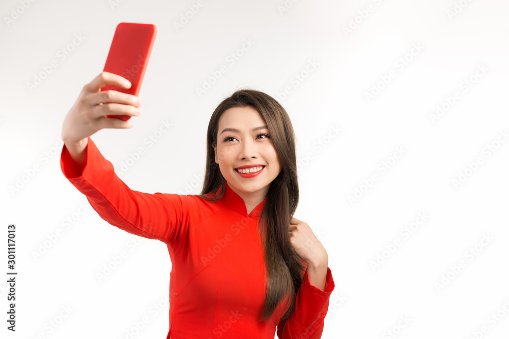 Asian woman in Vietnamese dress traditional ao dai. Beautiful toothy smiling young woman using smartphone doing FaceTime with friends against white background. Asian woman in Vietnamese dress traditional ao dai. Beautiful toothy smiling young woman using smartphone doing FaceTime with friends against white background.