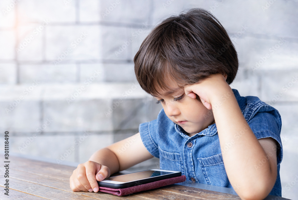 Portrait of Child boy playing playing game on mobile phone, Cute kid sitting outdoor cafe waching cartoons on cell phone while waiting for food. Children with Technology concept. Portrait of Child boy playing playing game on mobile phone, Cute kid sitting outdoor cafe waching cartoons on cell phone while waiting for food. Children with Technology concept.