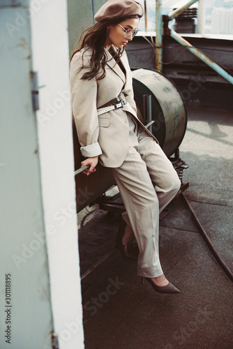 attractive stylish girl posing in beige suit and beret on urban roof