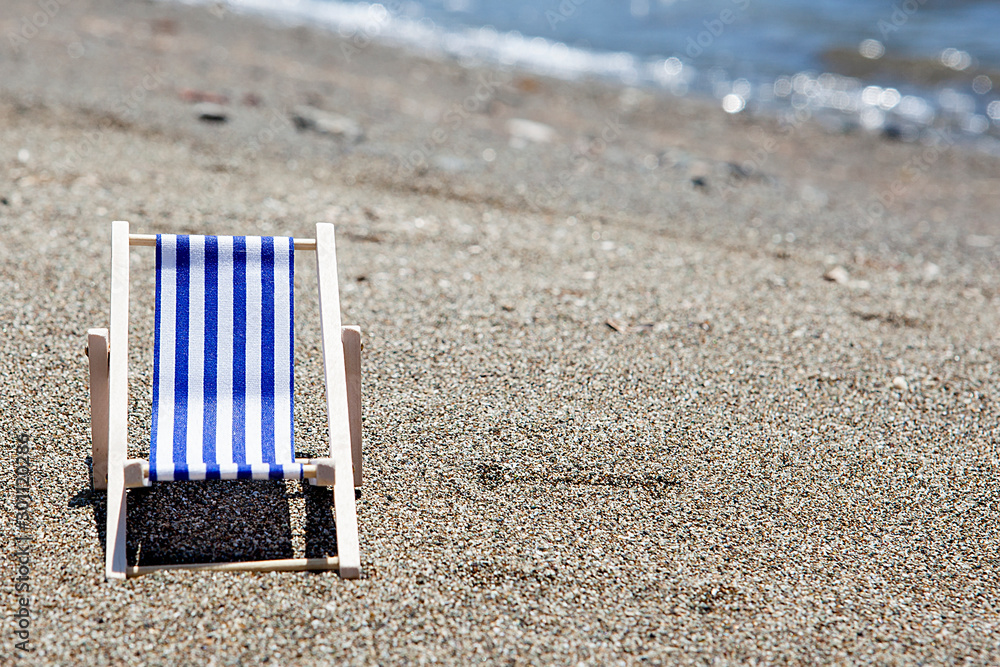 Toy chaise longue on sandy beach on sunny day at the blue sea background. Relaxation concept. Toy chaise longue on sandy beach on sunny day at the blue sea background. Relaxation concept.