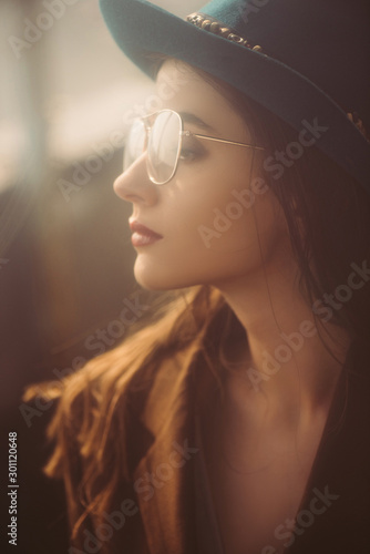 beautiful elegant woman posing in hat, eyeglasses and brown jacket on roof