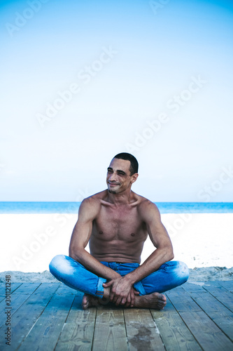 young muscular man in denim pants resting and posing on the beach © Victoria Key