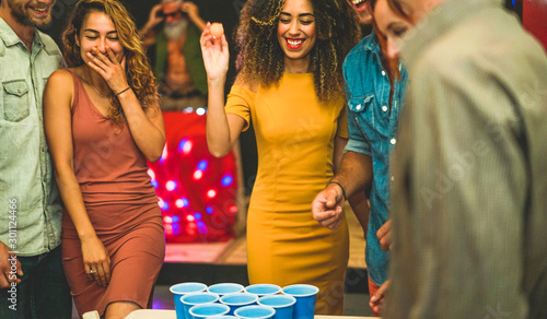 Group of happy friends playing beer pong in hostel bar - Young trendy people having fun doing party at night - Friendship, fest and nighlife concept - Focus on center girl face