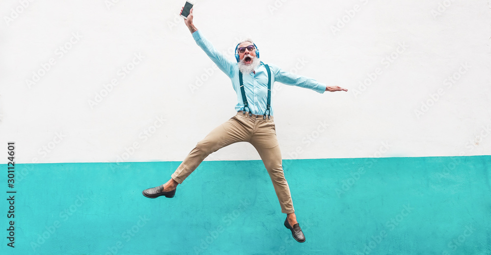 Senior crazy man jumping and listening music outdoor - Happy mature male celebrating and dancing outside - Joyful elderly lifestyle concept - Focus on his face
