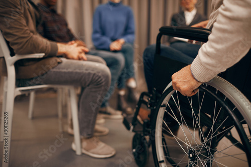 Close-up of senior disabled man sitting in wheelchair and visiting business meeting
