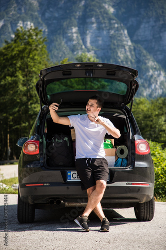 Young travel man sits in the car trunk take selfie photo on phone on mountaind background © F8  \ Suport Ukraine