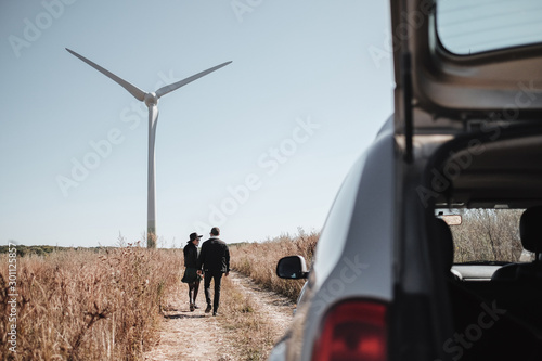 Happy Traveling Couple Enjoying a Car Trip on the Field Road with Electric Wind Turbine Power Generator on the Background