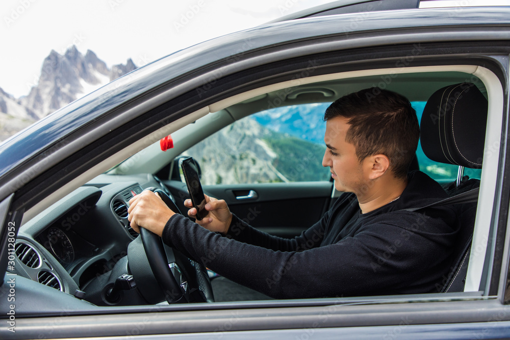 Young man driving and looking message in his smart phone. Young man driving and looking message in his smart phone.