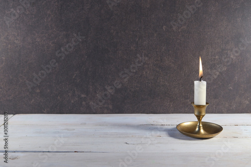 Wall Mural Burning candle in vintage metal candlestick on white wooden table and copy space on dark stone background