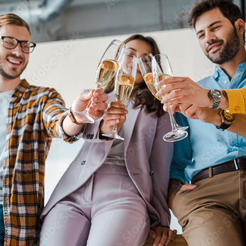 selective focus of cheerful businessmen and businesswomen toasting champagne glasses in office