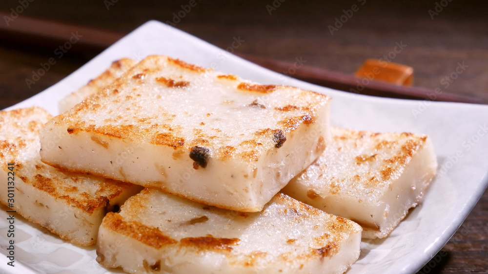 Pouring black soy sauce on ready-to-eat delicious turnip cake, Chinese traditional local dish radish cake in restaurant, close up, copy space. Pouring black soy sauce on ready-to-eat delicious turnip cake, Chinese traditional local dish radish cake in restaurant, close up, copy space.