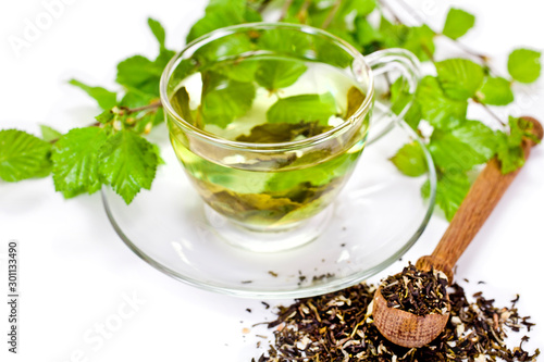 Glass cup of green tea with green natural birch branches and dry tea in a wooden spoon isolated on a white background. 