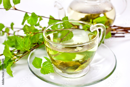 Glass cup of green tea with tea pot and green natural birch branches isolated on a white background. 