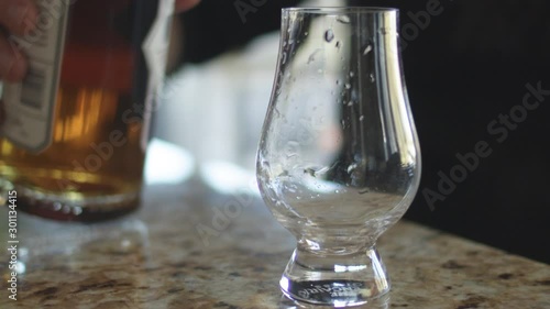 Man pouring whiskey into a glencairn glass on a countertop in slow motion. photo