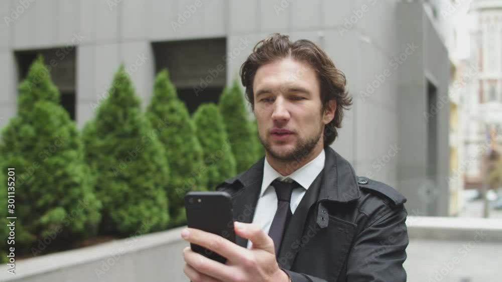 Focused businessman walks through the street and makes a video call. Man is talking to business partner thought video call. Focused businessman walks through the street and makes a video call. Man is talking to business partner thought video call.