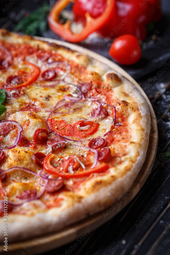 Pizza with sausages, ham, onions and tomatoes
