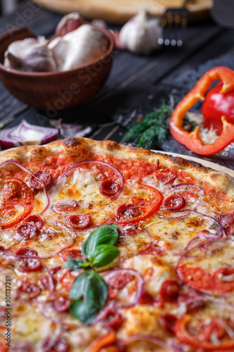 Aromatic pizza with hunting sausages, onions and tomatoes near with vegetables