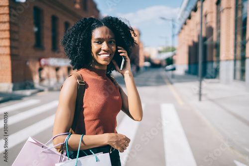 Portrait of cheerful millennial female teenager using smartphone gadget for making online international conversation and discussing sales of Cyber Monday, positive hipster girl using application