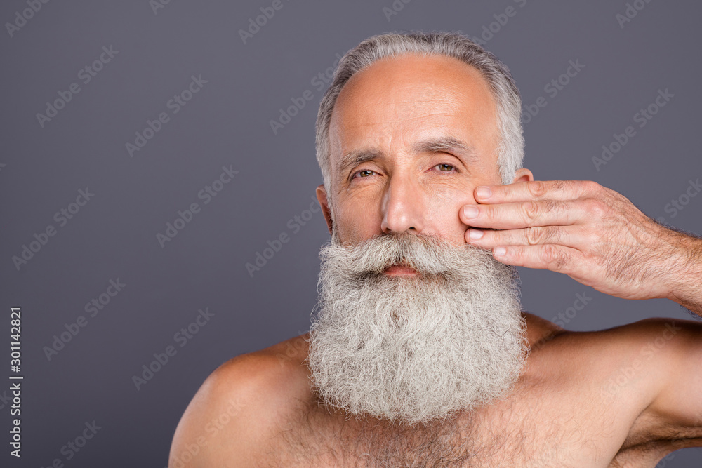 Obraz premium Close up photo of aged handsome man metrosexual touching facial skin applying anti age cream gel amazing neat long beard shirtless isolated grey background