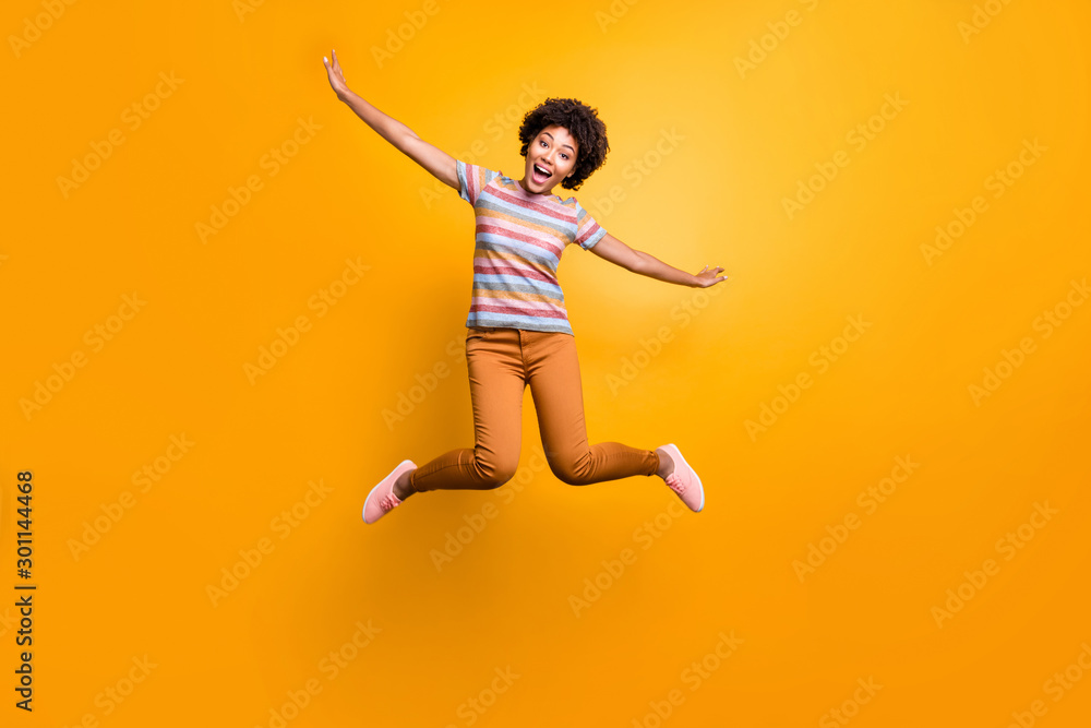 Full length body size photo of cheerful pretty girlish youngster with hands like spreading wings orange trousers striped t-shirt curly wavy isolated vivid color background