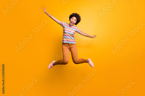 Full length body size photo of cheerful pretty girlish youngster with hands like spreading wings orange trousers striped t-shirt curly wavy isolated vivid color background © deagreez
