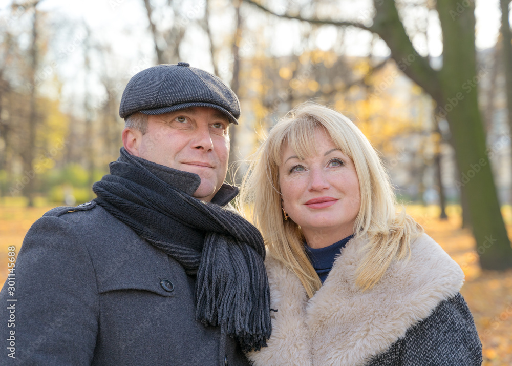 Closeup portrait of happy blonde mature woman and beautiful middle-aged brunette, look up to sky. Loving couple of 45-50 years old walks in autumn park in warm clothes Closeup portrait of happy blonde mature woman and beautiful middle-aged brunette, look up to sky. Loving couple of 45-50 years old walks in autumn park in warm clothes