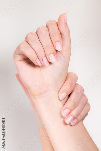 Closeup top view of two female hands with natural pink manicure made with modern gelpolish isolated on white background. Nude look nail design concept. Vertical color photography.