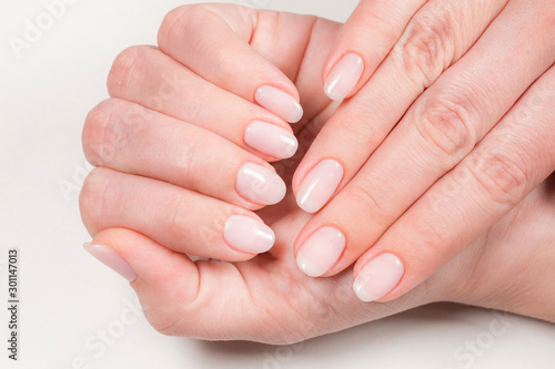 Closeup top view of two female hands with natural pink manicure isolated on white background. Nude look nail design concept. Horizontal color photography.