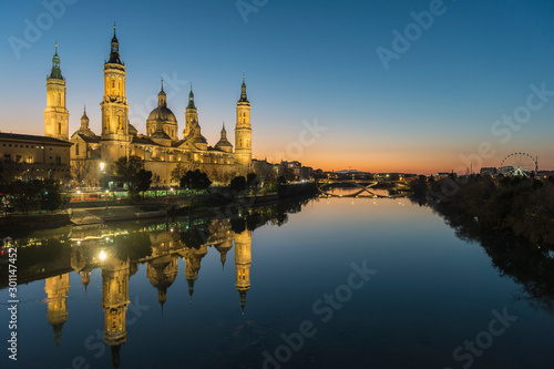 View of the cathedral of El Pilar de Zaragoza (Spain) next to the river Ebro, at dusk. © cmassway