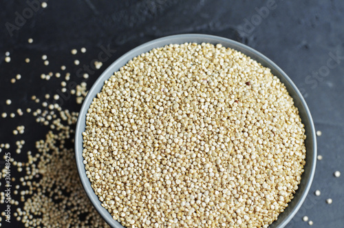Dry organic quinoa seeds in gray ceramic bowl on dark concrete background