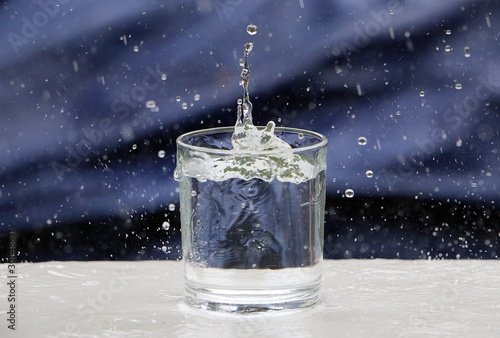 raindrops fall into a glass of water that stands on the table in the garden