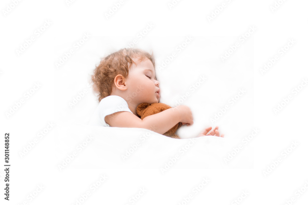 Little baby kid sleeps on a clean bedspread hugging a teddy bear. Caucasian child girl boy sitting dreams on big bed, white background Little baby kid sleeps on a clean bedspread hugging a teddy bear. Caucasian child girl boy sitting dreams on big bed, white background