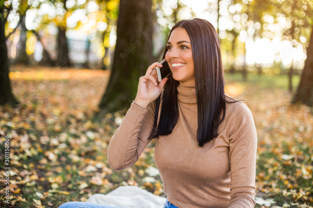 Beautiful woman talking on the phone while sitting in the park and enjoys in autumn. Beautiful woman talking on the phone while sitting in the park and enjoys in autumn.
