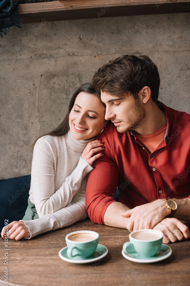 smiling tender young couple hugging and drinking coffee in coffee shop smiling tender young couple hugging and drinking coffee in coffee shop